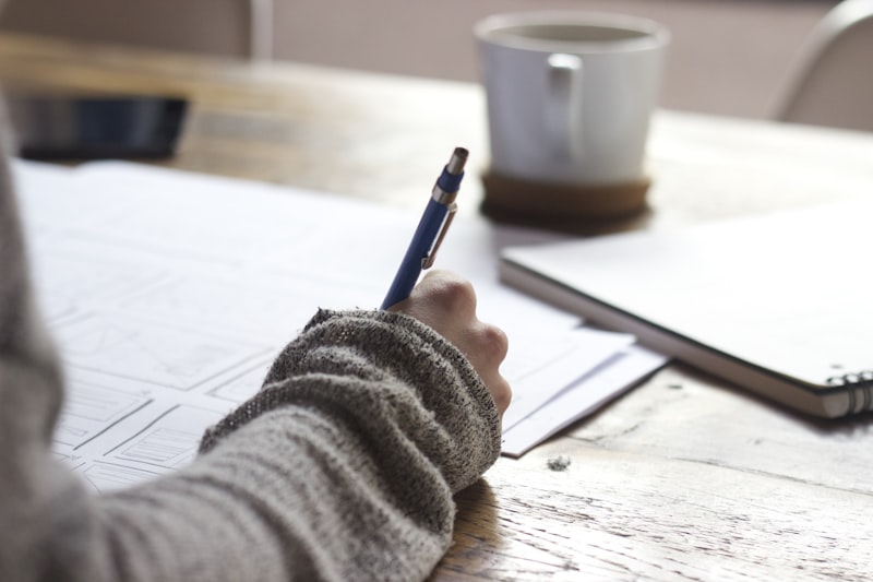 Hand writing notes with a pen in an open notebook on a desk